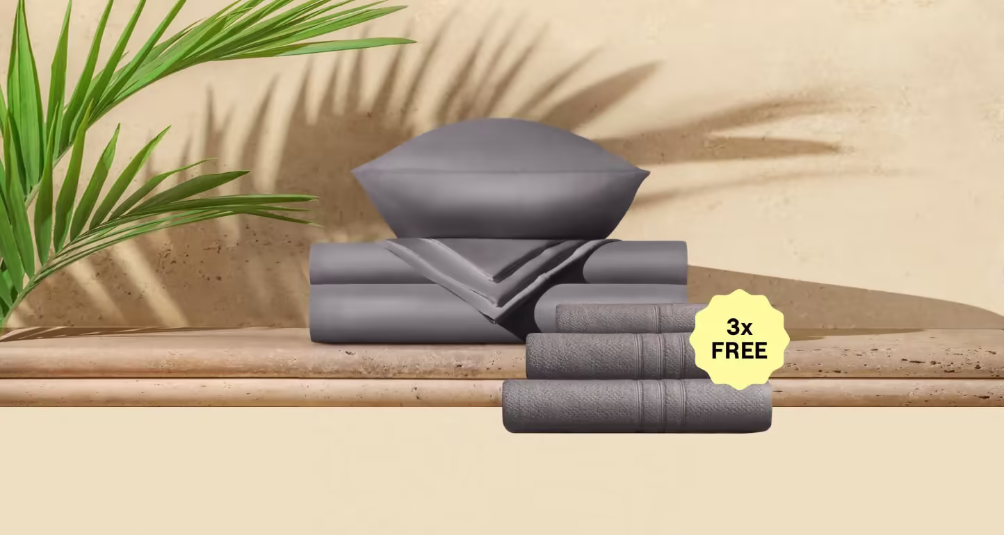 Stone grey sheet set folded with rolled towels on a bed
